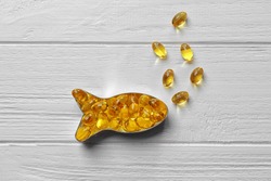 Capsules of cod liver oil arranged in a fish shape on white wooden background