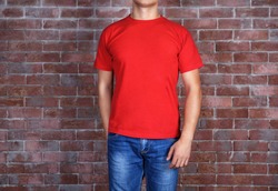 Handsome young man in blank red t-shirt standing against brick wall, close up