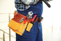 Worker with tools belt on light background, close up view