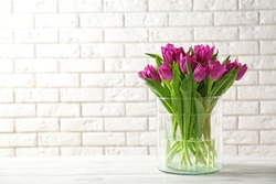 Glass vase with bouquet of beautiful tulips on brick wall background