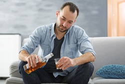 Handsome depressed man drinking whisky at home