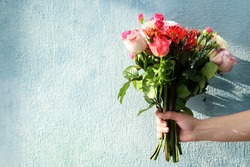 Woman hand holding bouquet of fresh flowers on light background