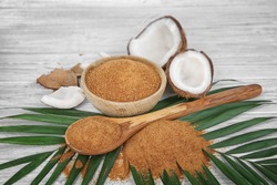 Bowl and spoon of brown sugar with coconut on wooden background