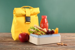Lunch box with appetizing food and bag on wooden table against chalkboard background