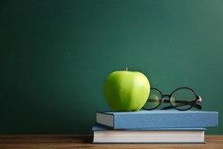 Books and apple on chalkboard background