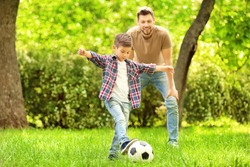 Dad and son playing football together on green meadow