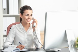 Young female receptionist talking on phone in office