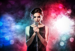 Young woman with microphone and colorful lights on concert