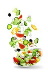 Sliced vegetables falling into bowl with salad on white background