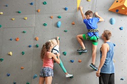 Instructors helping children climb wall in gym