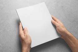 Man holding brochure with blank cover on grey background. Mock up for design