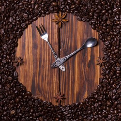 Clock made of coffee, teaspoon, dessert fork and anise on dark wooden background