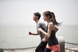 young asian man and woman running jogging outdoors by the sea, side view