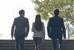 rear view of three young successful asian business people ascending steps
