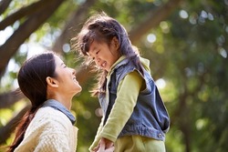 young asian mother sitting on grass in park having a pleasant conversation with cute daughter