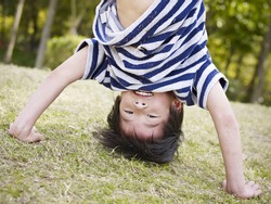 little asian boy playing upside down on grass in a park.