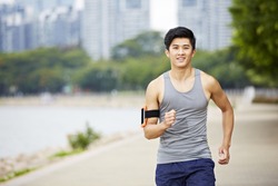 young handsome asian jogger running exercising in city park wearing fitness tracker