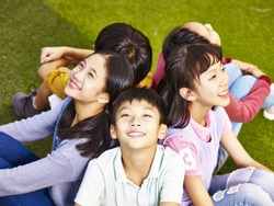 group of asian elementary school boys and girls sitting on playground grass looking up at the sky