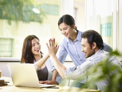 young asian business person giving coworker high five in office celebrating achievement and success.