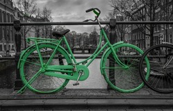 Green bike isolated on black and white over an Amsterdam canal. Very moody sky in background.