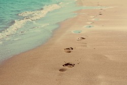 footprints on sand beach along the edge of sea - vintage retro style