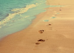footprints on sand beach along the edge of sea - vintage retro style