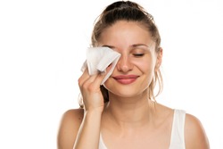 A smiling woman cleans makeup from her face with wet wipes on a white background