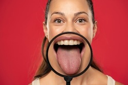 Young happy woman showing her healthy tongue through a magnifying glass