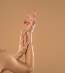 Cropped shot of woman applying cosmetic product on her hands on a beige background. Young woman applying hand cream.