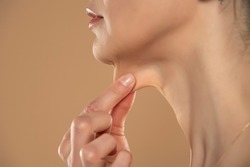 A close-up and side profile view of a caucasian lady pinching the loose skin at the front of her throat. Commonly called a turkey neck and corrected with a platysmaplasty.