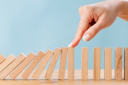Business woman's finger try to stopping falling wooden dominoes blocks for business solution concept. Business crisis effect or risk protection concept