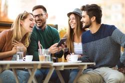 Group of four friends having a coffee together. Two women and two men at cafe talking laughing and enjoying their time using digital tablet.