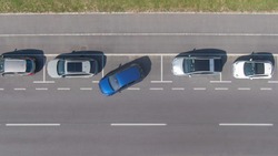 DRONE, TOP DOWN: Flying above a shiny blue car driving out of a roadside parking space. Modern vehicle leaves a parking spot in a long line of parked cars next to an empty city street in Ljubljana.