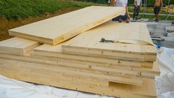 CLOSE UP: Cross-laminated timber wall panels lie on the ground next to a group of unrecognizable workers. A stack of CLT wall panels lie uncovered at a construction site of a modern housing project.