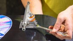 CLOSE UP: Young man firming and screwing the nut on bolt of skateboard trucks with wrench. Mistake at bolting trucks on skate deck for mounting wheels. Assembling parts for new skateboarding setup.