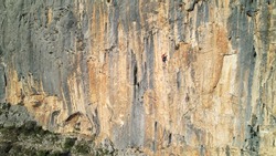 AERIAL: Gorgeous sunlit limestone wall with ascending young female rock climber. Adrenaline outdoor activity in breathtaking and picturesque surroundings. Rock climber on the way up of canyon wall.