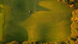 AERIAL, TOP DOWN: Farm tractor with hay tedder turning over mowed hay in autumn. Farmer aerating grass to speed up drying at sunrise on an autumn morning. Preparing fodder for cows in fall season.