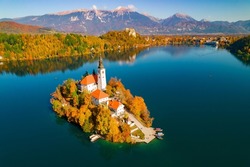 AERIAL: Picturesque alpine Lake Bled with island and church in autumn shades. Gorgeous Bled island with church in embrace of vivid autumn trees. Beautiful fall season creating picturesque views.