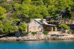 Lovely traditional stone house under lush green pine trees by the Adriatic Sea. Idyllic location of an empty summer beach house on rugged rocky seashore. Gorgeous hidden gems on sunny island of Hvar.