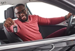 Happy handsome african man showing car keys in his newly bought auto smiling cheerfully sitting in the  luxury vehicle copyspace owner ownership sales driving consumerism private taxi concept