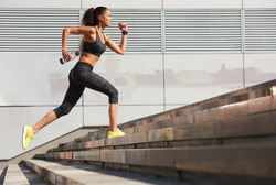 Athletic woman running up to the stone stairs with bottle of water in City  with fitness tracker