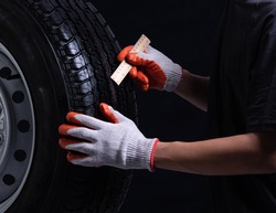 Auto mechanic checking a car tire on a black background,wood ruler measure the tread 