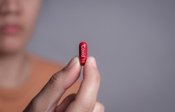 Female hand holding a medical red capsule pill between fingers against gray background,Coronavirus,Covid-19 Cure,Anti-Covid 19,anti flu drug pill