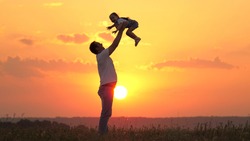 Dad tosses his happy daughter into blue sky at sunset. Father and healthy child play together, laugh and hug. Carefree kid flies into sky. Child is in the arms of parent. Dad's day off. Happy family