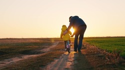 Father teaches a little kid girl to ride a child's bike on the road, in the fall, in spring. Happy family, childhood. Happy family, dad teaches his daughter, child to ride a bike in the park at sunset