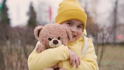 Kid plays with teddy bear in park in spring. Little girl hugs her favorite teddy bear on playground. Plush toy in hands of kid in autumn park. Child plays with toy. Best friends. Family, childhood