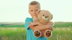 Kid plays with toy bear, looking at camera. Happy family. Plush toy in hands of boy, child in summer park. Cute baby boy hugs his favorite soft teddy bear on playground. Kid plays with Teddy bear