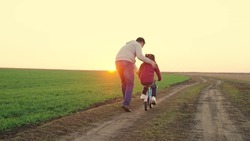 Father teaches little kid girl to ride child's bike on road, in fall, in spring. Happy family, dad teaches his daughter, child to ride bike in park at sunset. Happy family, childhood. Parent, child