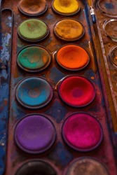 Set of old used watercolor paints close-up artistic background. One of art tools: color palette dark pattern backdrop.