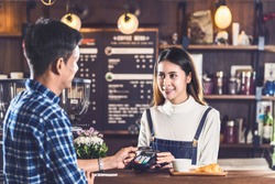 Asian customer man paying with credit card via contactless nfs technology to Asian Barista of Small business owner at the table in coffee shop, Small business owner and startup in coffee shop concept